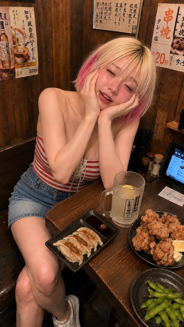 Young woman with blonde and pink hair posing playfully at a Japanese izakaya table with food and beer.