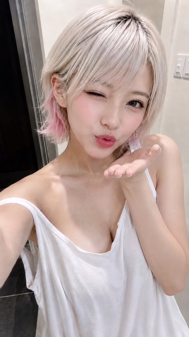 Young woman with short platinum blonde and pink hair taking a close-up selfie while winking and blowing a kiss.