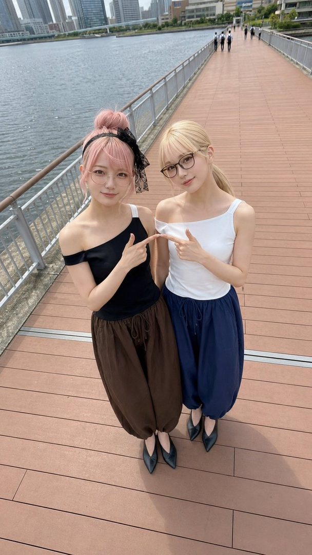 Two young women with pink and blonde hair posing together on a wooden riverside boardwalk in an urban setting.