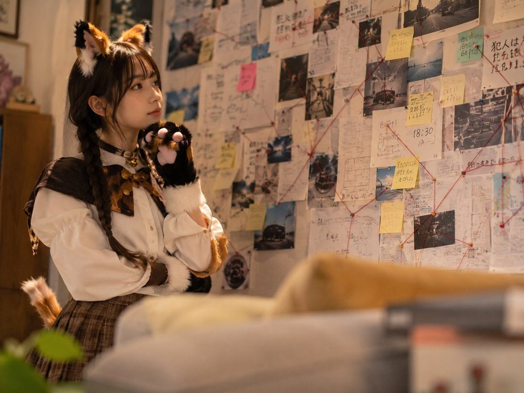 Young woman in detailed three-colored cat Holmes cosplay standing before a detective investigation board covered in photos, notes, and red strings.