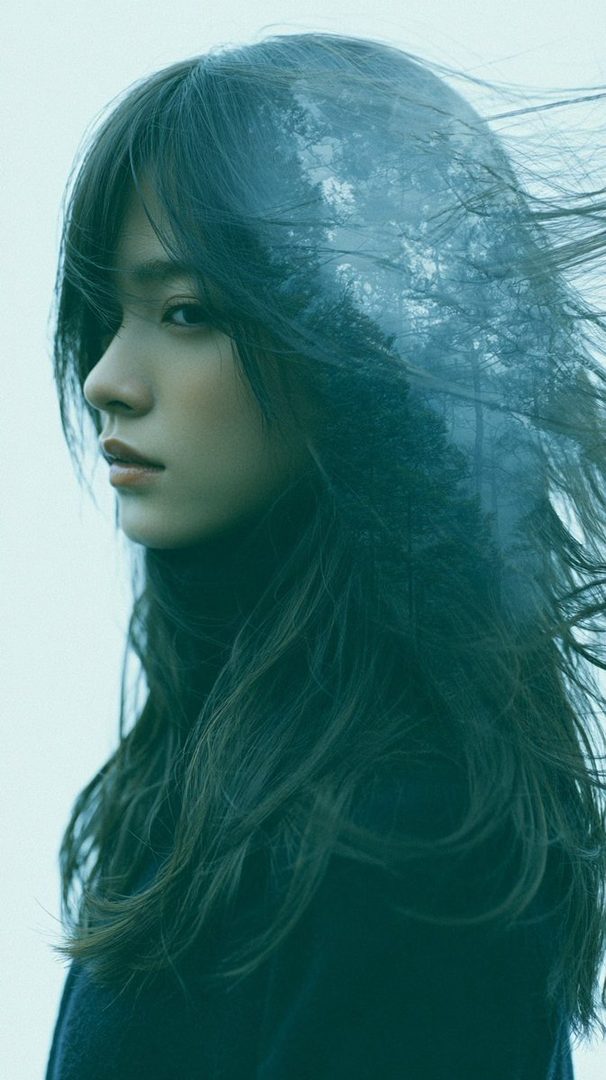 A double exposure portrait of a woman with long dark hair, overlaid with a forest scene, creating a dreamy and mysterious atmosphere.
