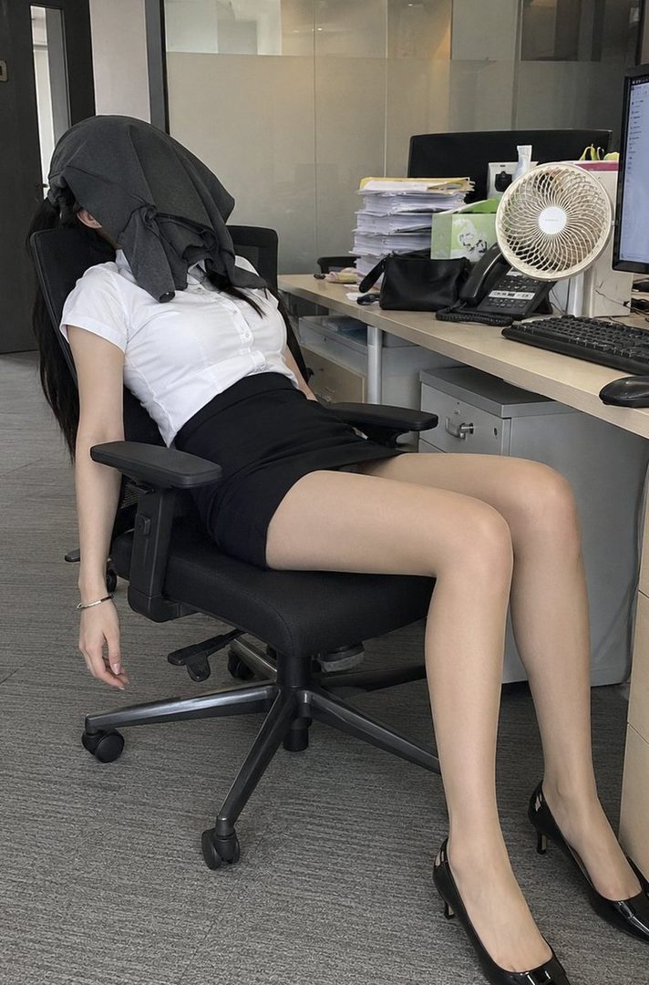 Exhausted young woman in white blouse and black skirt resting in an office chair with a jacket over her head.