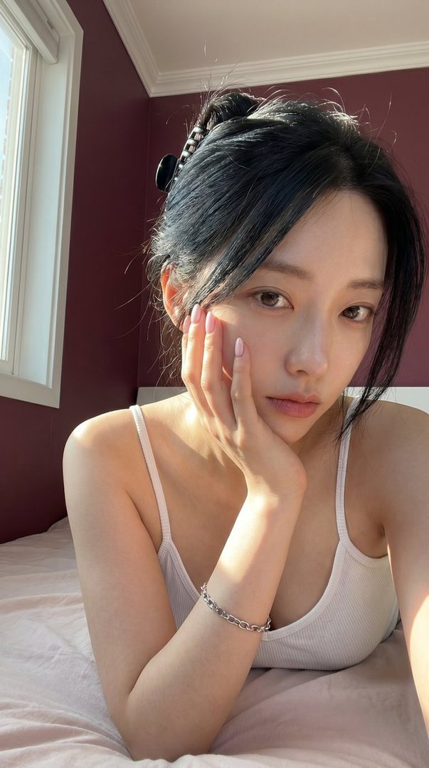 A woman with black hair in a white tank top lies on a bed, illuminated by natural light from a window.