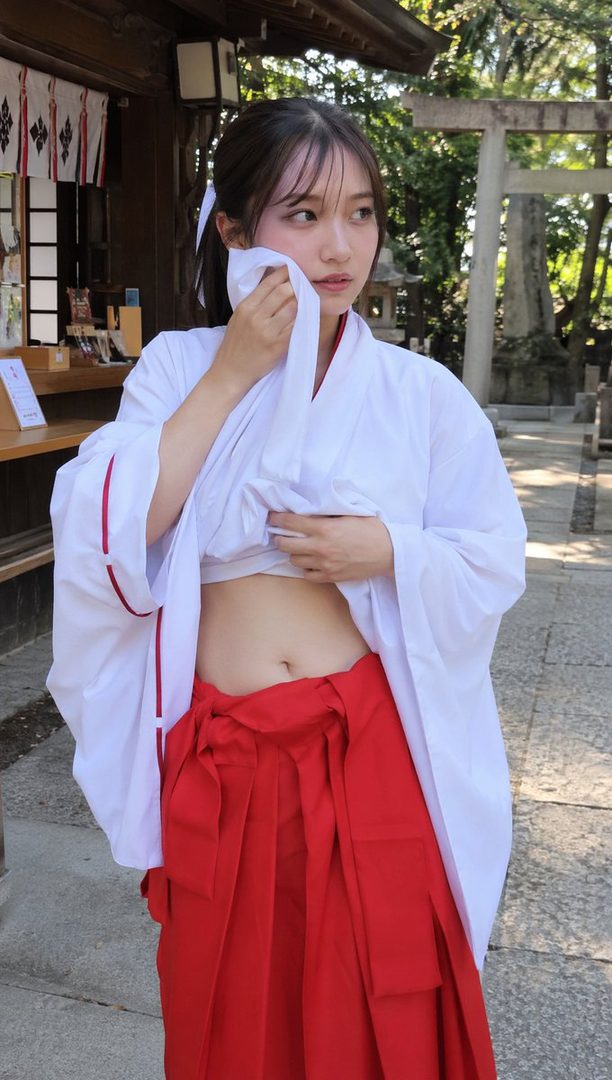 A young woman dressed as a miko (shrine maiden) in a white top and red hakama, wiping her face with a cloth, standing outdoors at a Japanese shrine.