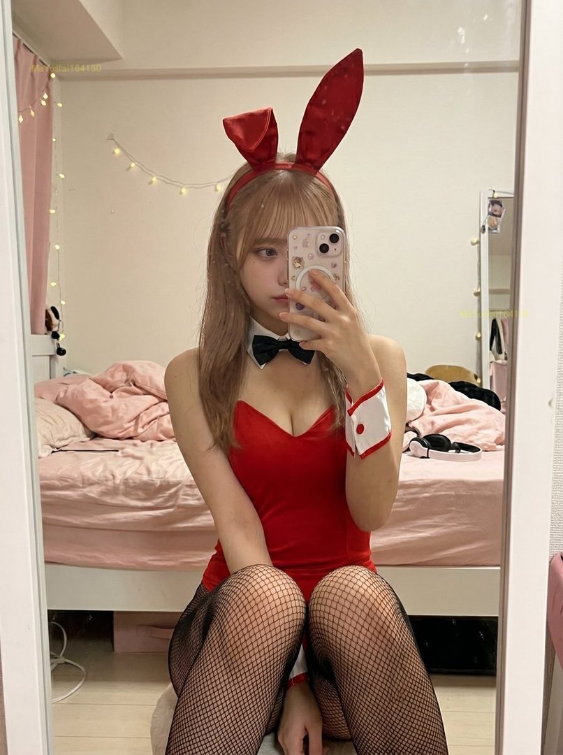 A woman in a red bunny costume takes a mirror selfie in a bedroom.
