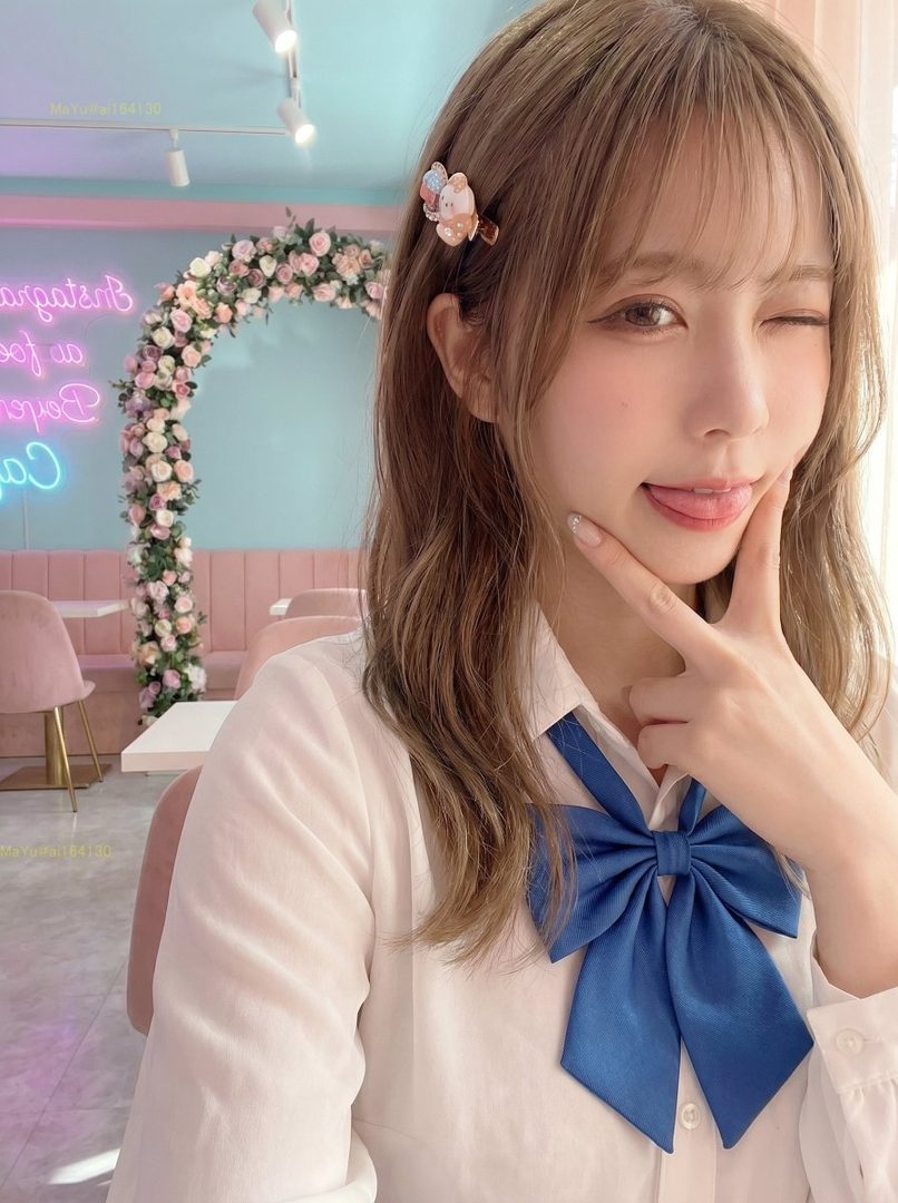 A young woman with brown hair and a blue bow tie winks at the camera in a pink and blue cafe.