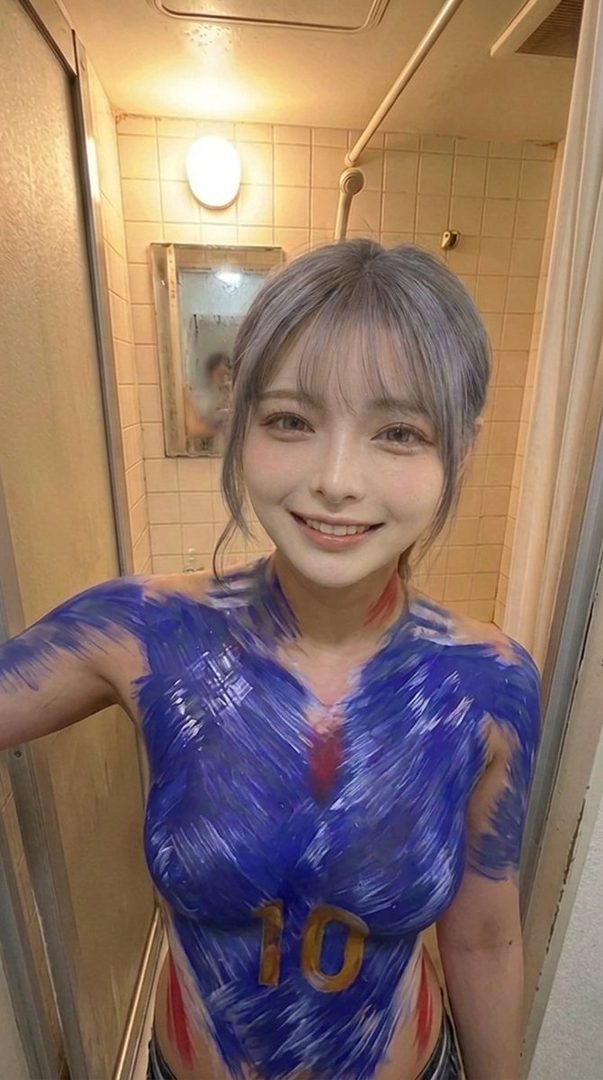 A woman with silver hair and bangs smiles at the camera, her torso painted with blue and red body paint resembling a sports jersey with the number 10.