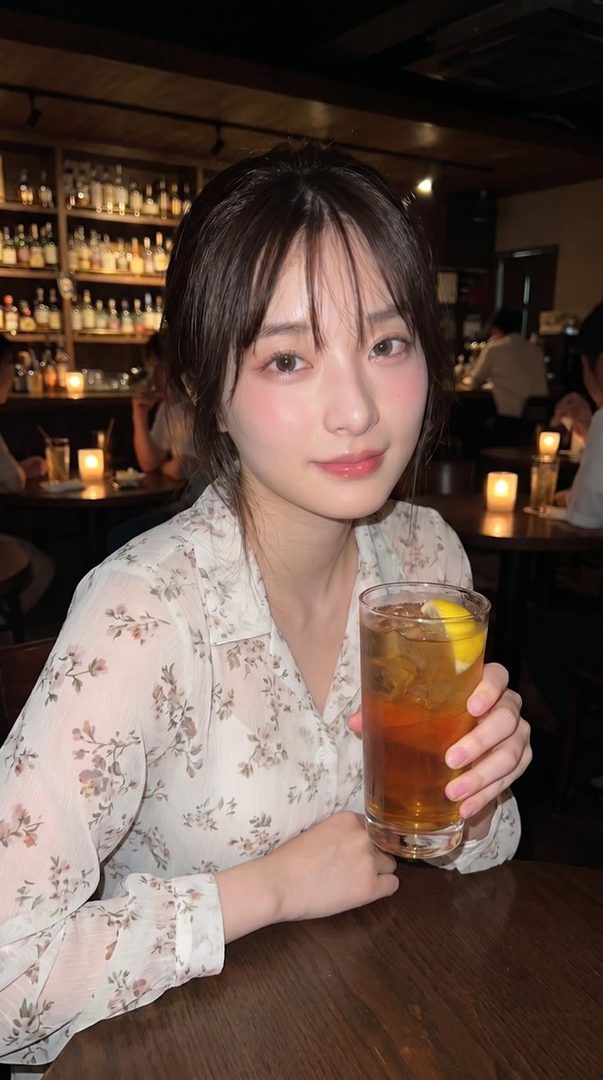 A cute woman with brown hair and bangs, wearing a floral blouse, holds a drink in a dimly lit bar.