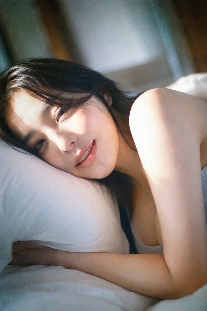 A serene woman with long dark hair lies on a white pillow, illuminated by natural light.