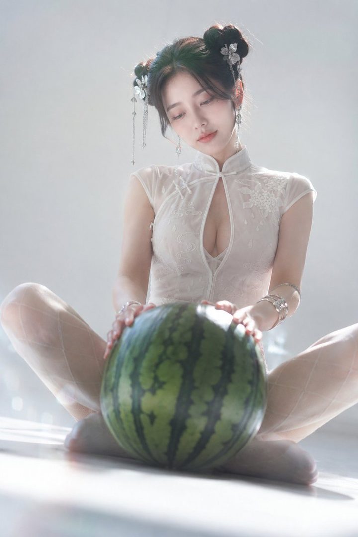 A woman in a white cheongsam with decorative hair buns holds a watermelon while sitting on the floor.
