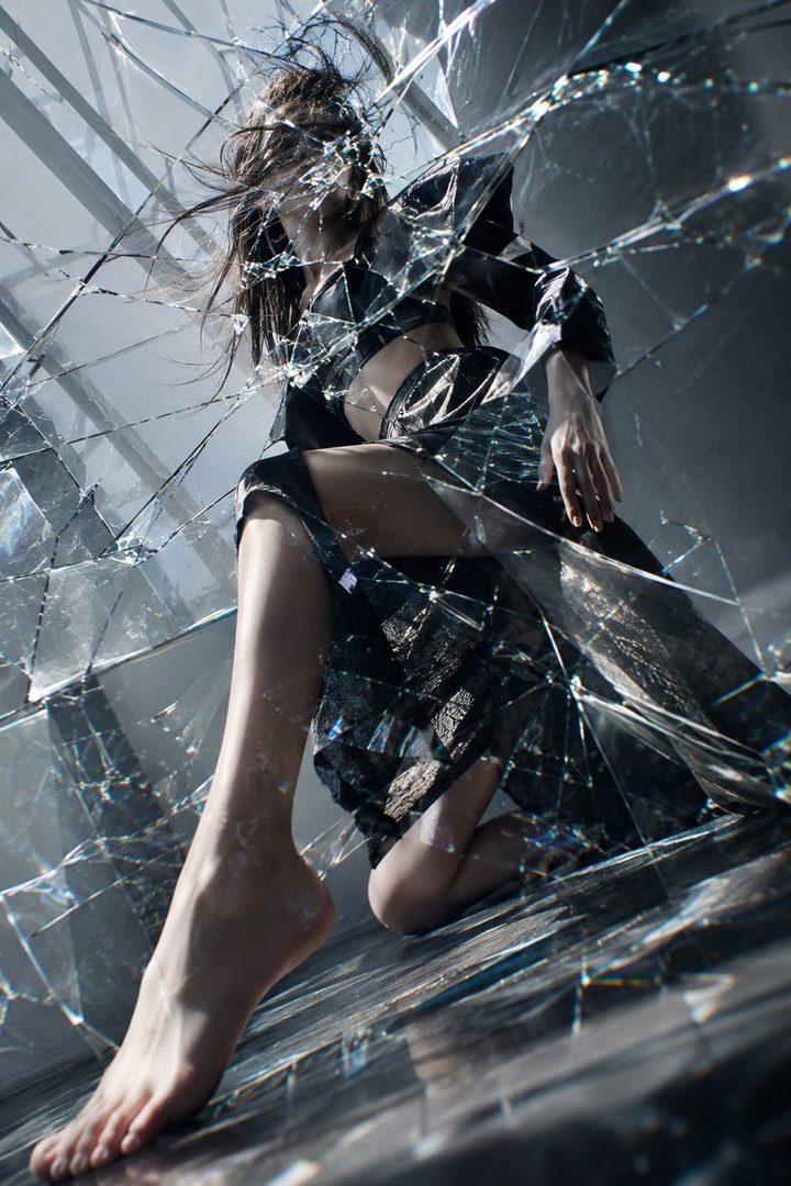 A woman with long brown hair is depicted through shattered glass, wearing a dark dress.