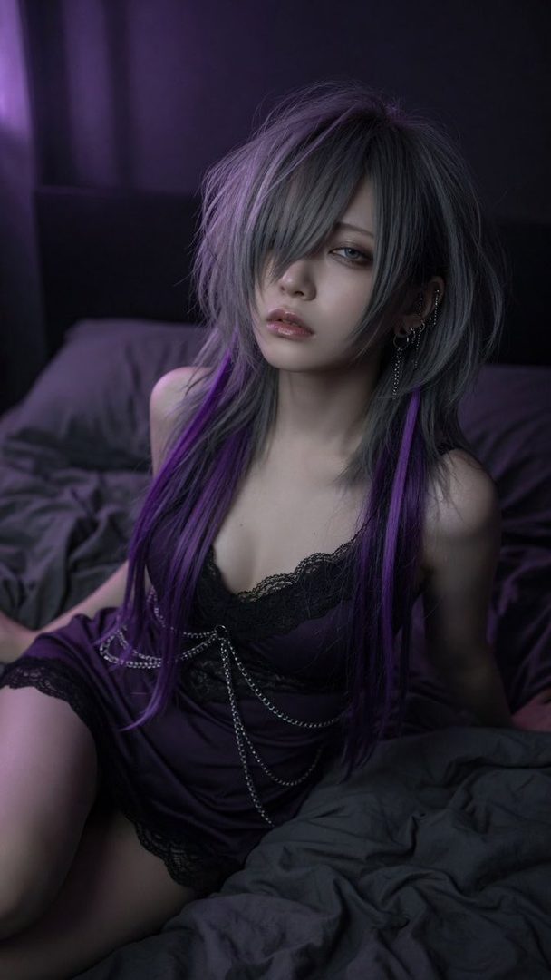 A woman with silver and purple hair wearing a dark purple slip dress with chains, lying on a bed in a dimly lit room.