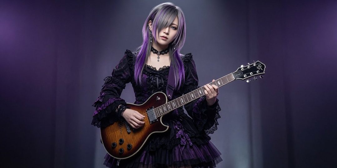 A woman with purple and grey hair wearing a gothic-style dress plays an electric guitar in a studio setting.