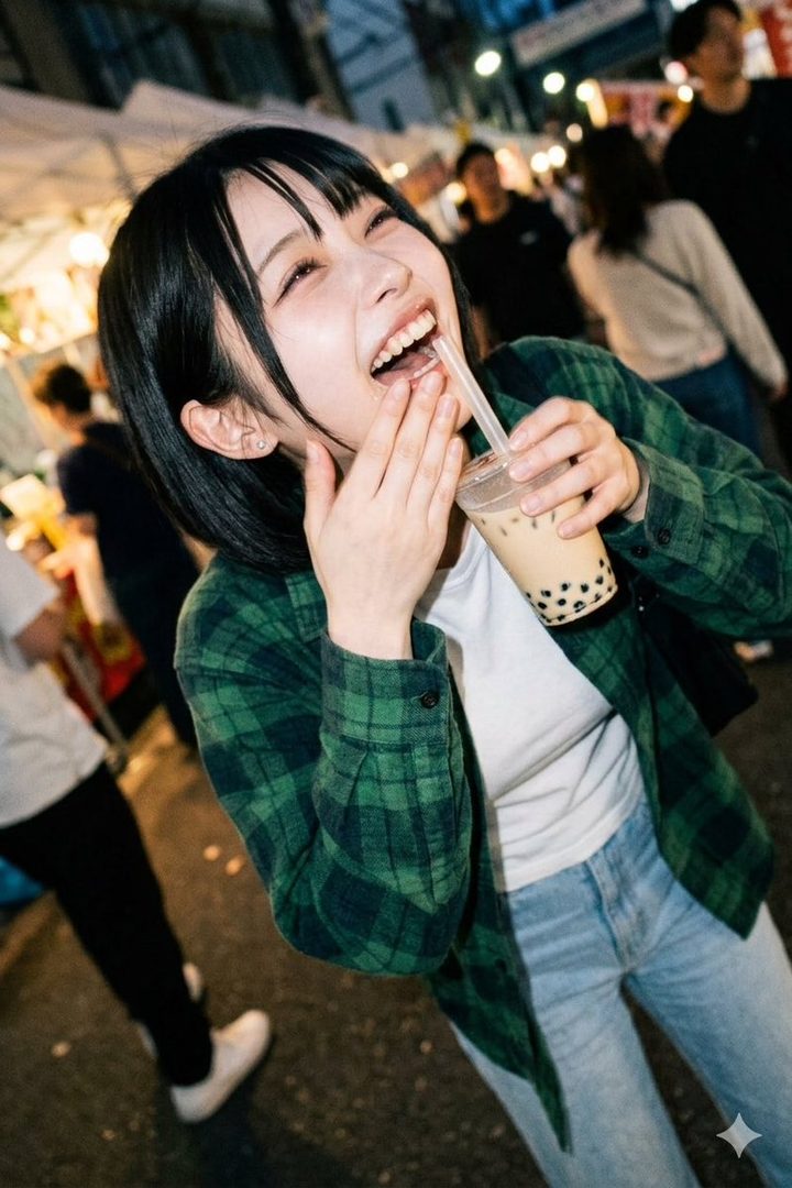 A young woman with short black hair and bangs, wearing a green plaid shirt, laughs while drinking bubble tea on a lively street at night.