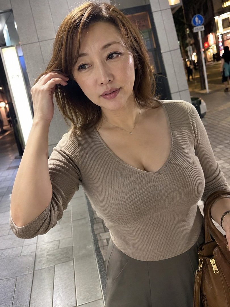 A woman with brown hair wearing a fitted knit top poses on a city street at night.