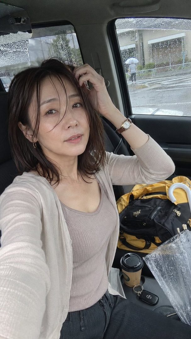 A woman with short brown hair takes a selfie inside a car on a rainy day.