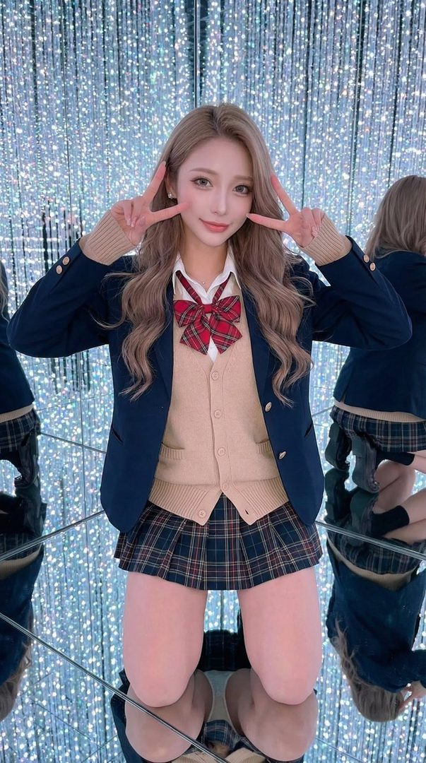 A young woman in a Japanese school uniform poses with peace signs in a sparkling light room.