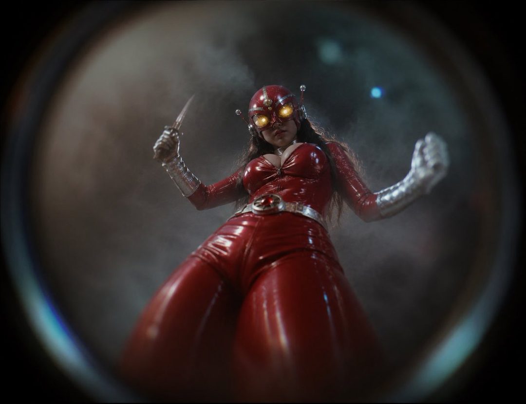 A woman in a shiny red superhero costume with glowing eyes and silver gloves holds a knife, viewed from a low angle.