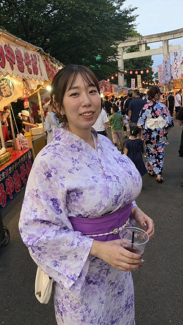 A young woman in a purple floral yukata smiles while holding a drink at a lively night market.