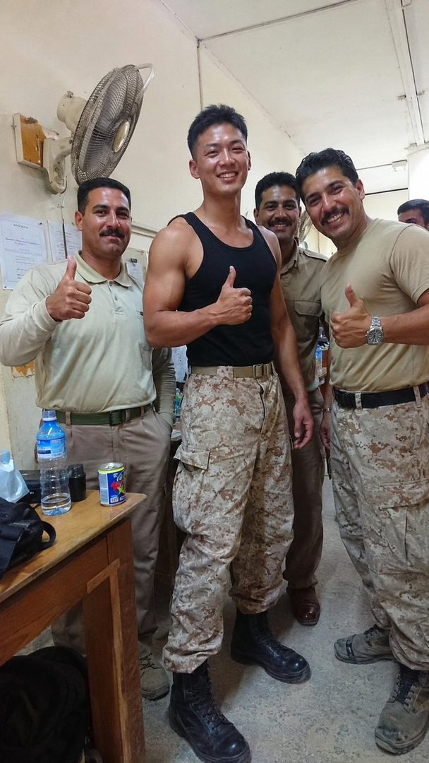 A group of men, some in military-style uniforms, giving thumbs up indoors.