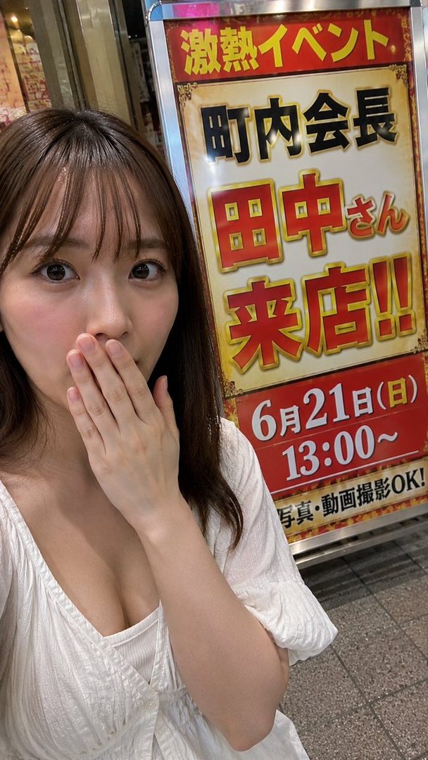A young woman takes a selfie in front of a Japanese event sign, covering her mouth with her hand.