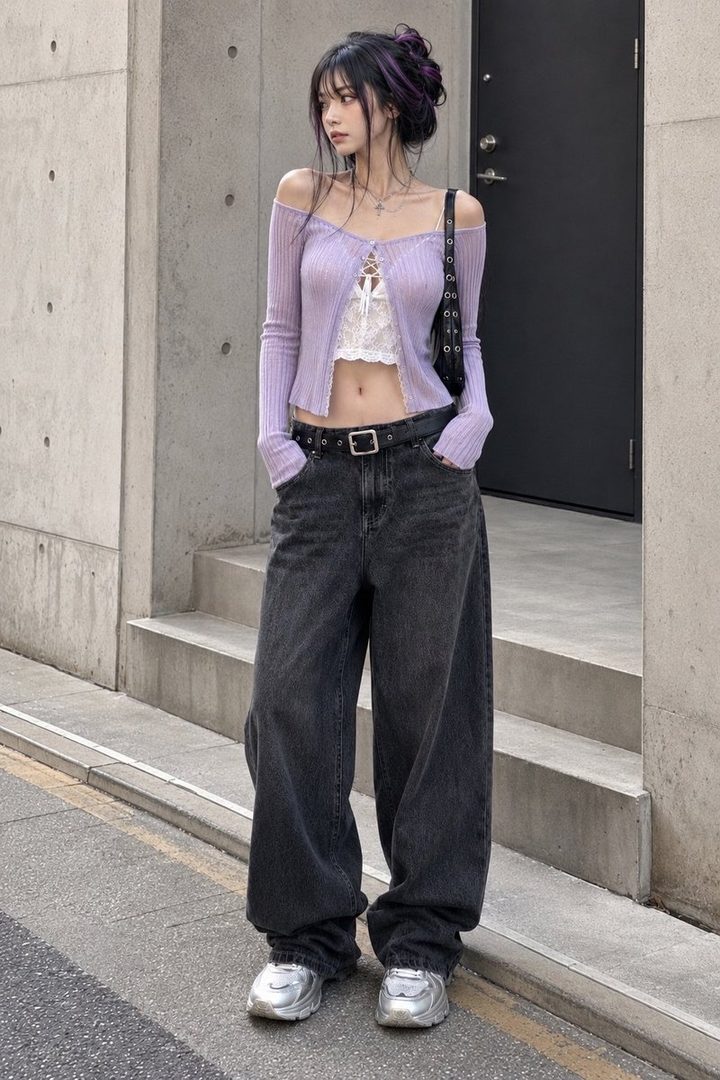 A young woman with dark hair and purple highlights wears a light purple off-the-shoulder cardigan, a white lace crop top, and baggy dark jeans with silver sneakers, standing on a street.
