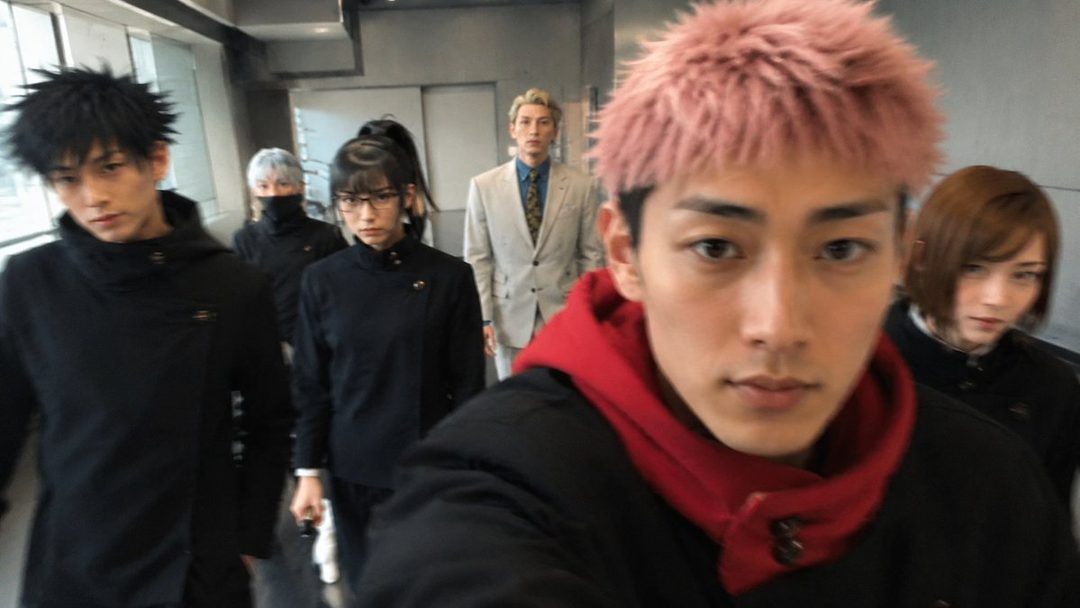 A group of people in cosplay, including a man with pink hair in the foreground, walking indoors.