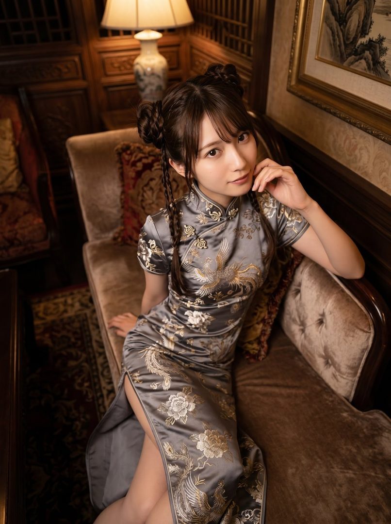 A woman in a grey cheongsam with gold embroidery sits on a sofa in a dimly lit room.