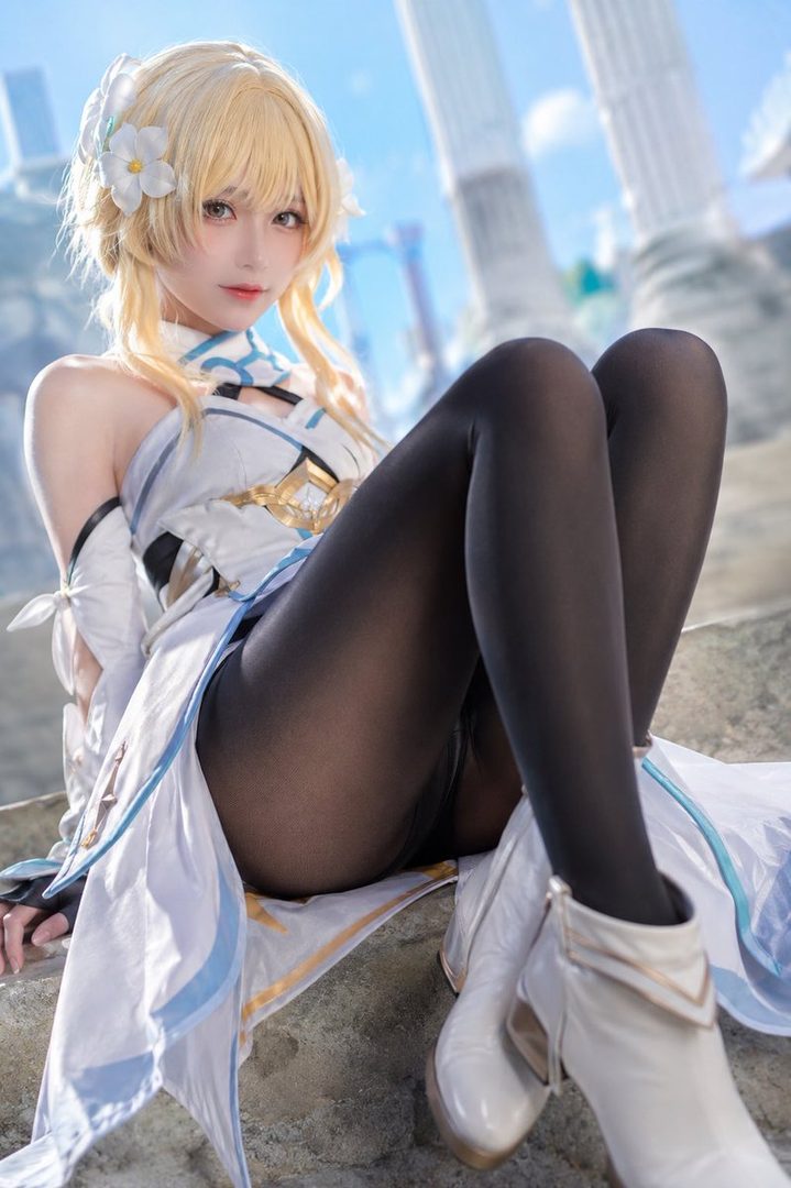 A blonde woman in a white and blue dress and black tights poses outdoors, looking at the camera.