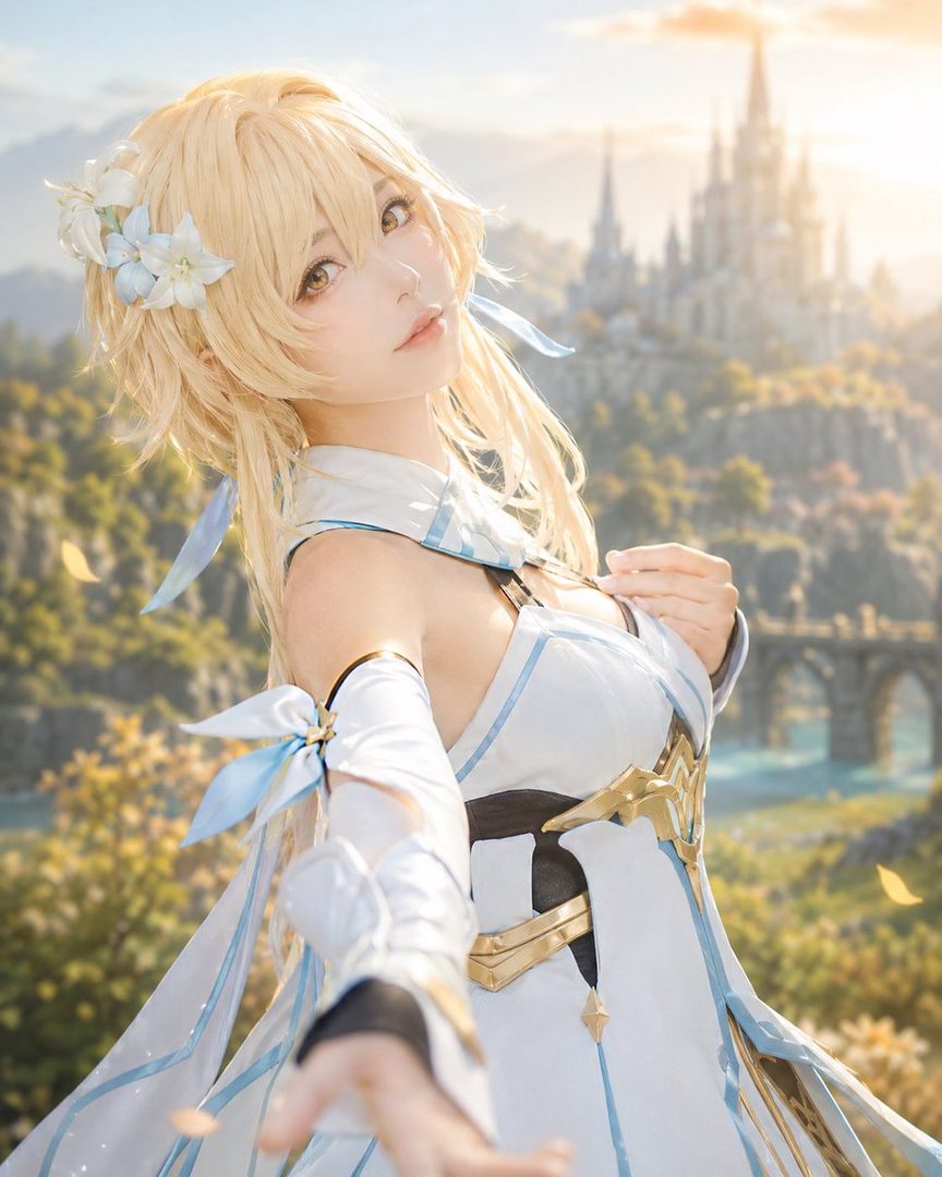 A blonde woman in a white and gold dress with blue accents, cosplaying as a character from Genshin Impact, stands in a fantasy landscape with a castle in the background.