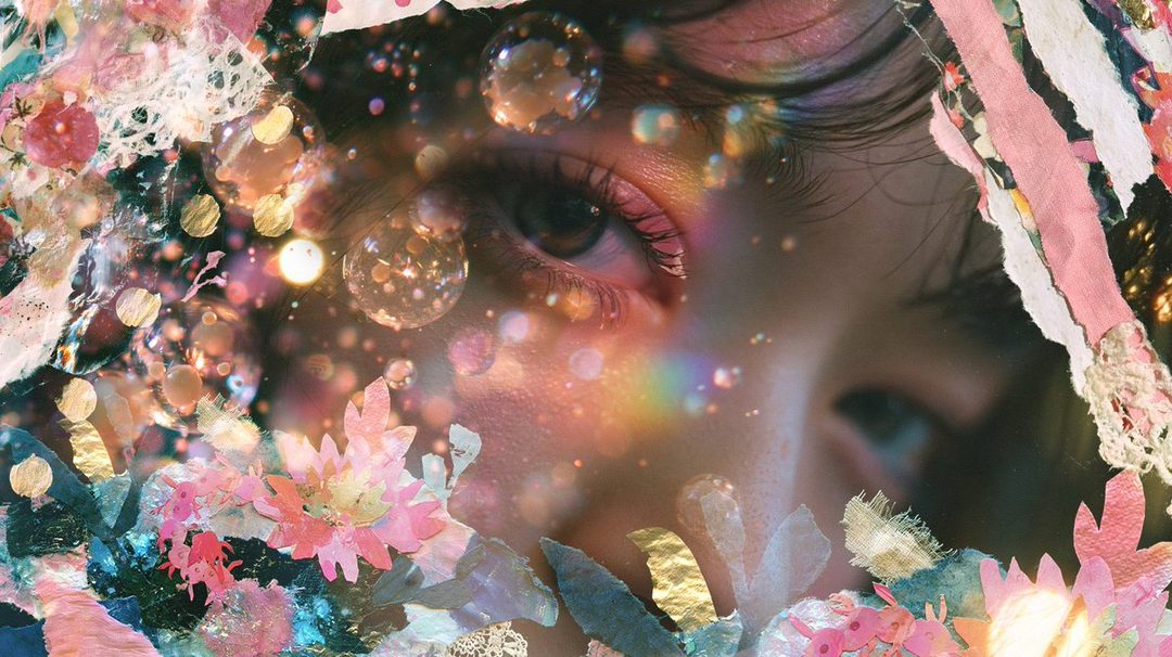 A close-up portrait of a person's eye surrounded by colorful, abstract floral and glittery elements, creating a dreamy and artistic effect.