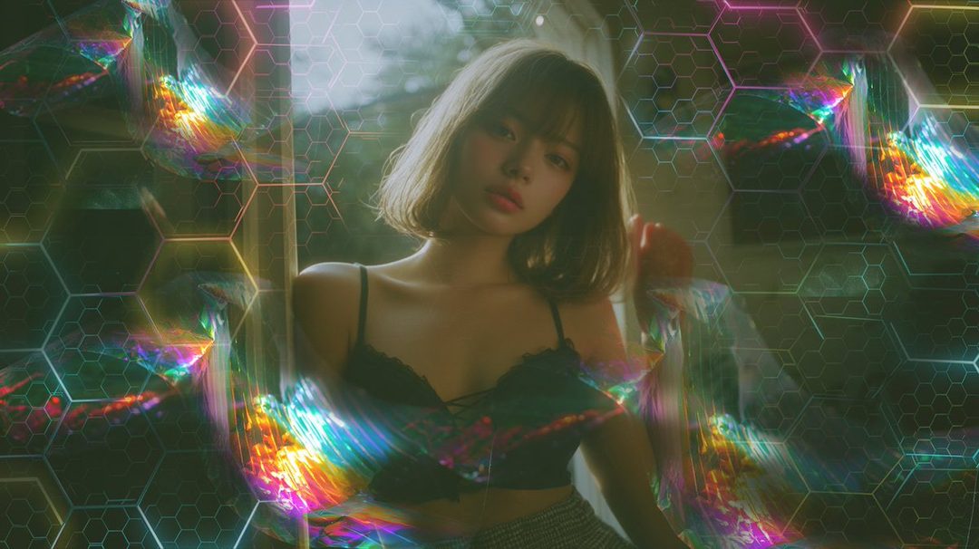 A dreamy portrait of a young woman with short brown hair, wearing a black lace top, with colorful light refractions and hexagonal patterns overlaid on the image.