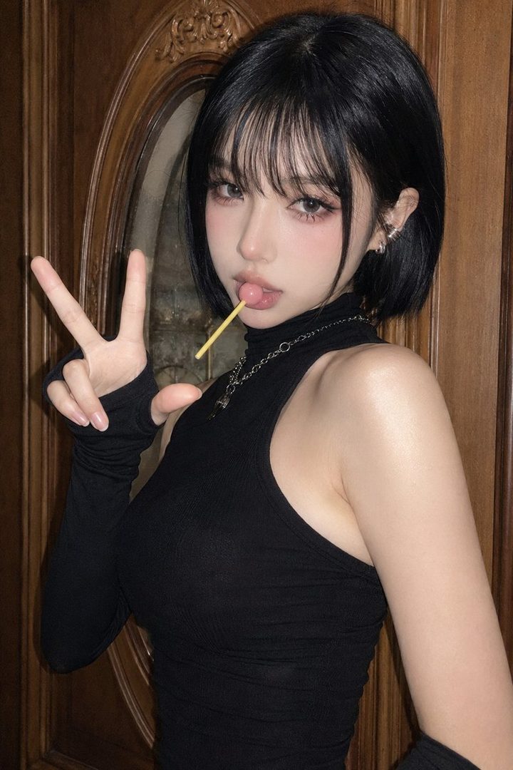 A young woman with short black hair and bangs poses with a lollipop in her mouth and a peace sign, wearing a black knit top.