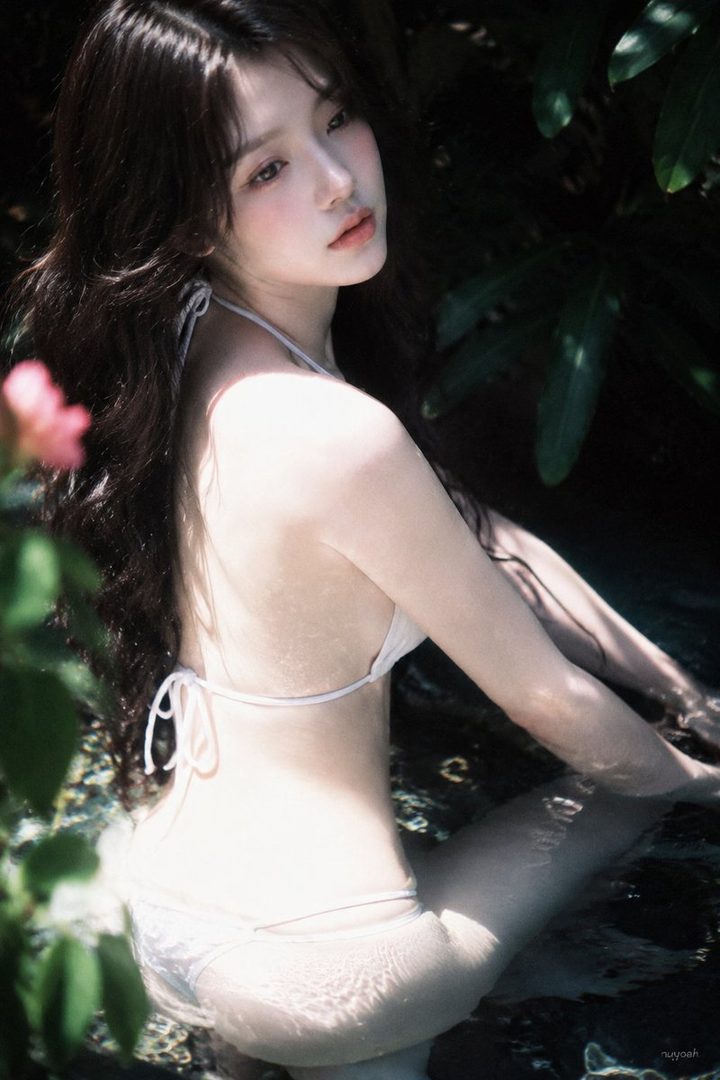 A beautiful East Asian woman with long brown hair is seen from behind, wearing a white bikini and partially submerged in water, surrounded by lush green foliage.