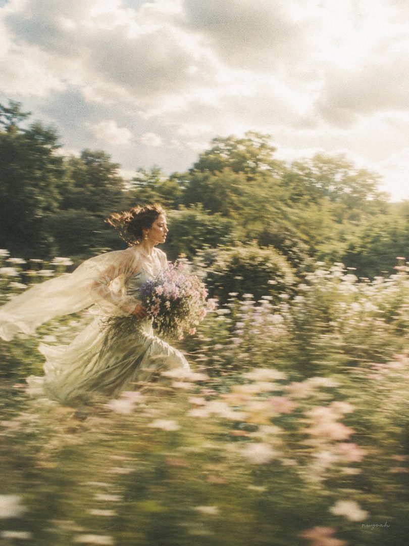 A woman in a flowing dress runs through a flower garden, holding a bouquet of flowers, with a dreamy and cinematic motion blur effect.
