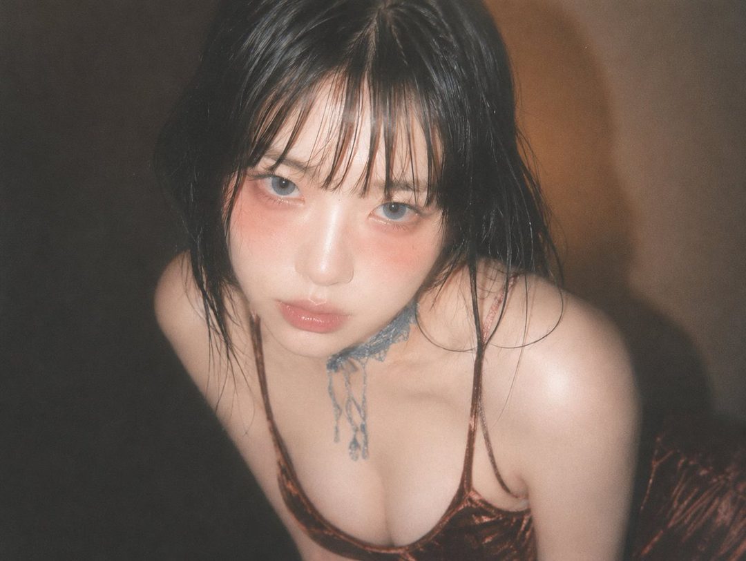 A close-up portrait of a young East Asian woman with black hair and bangs, wearing a reddish-brown velvet top and a blue lace choker, looking directly at the camera with a dreamy expression.