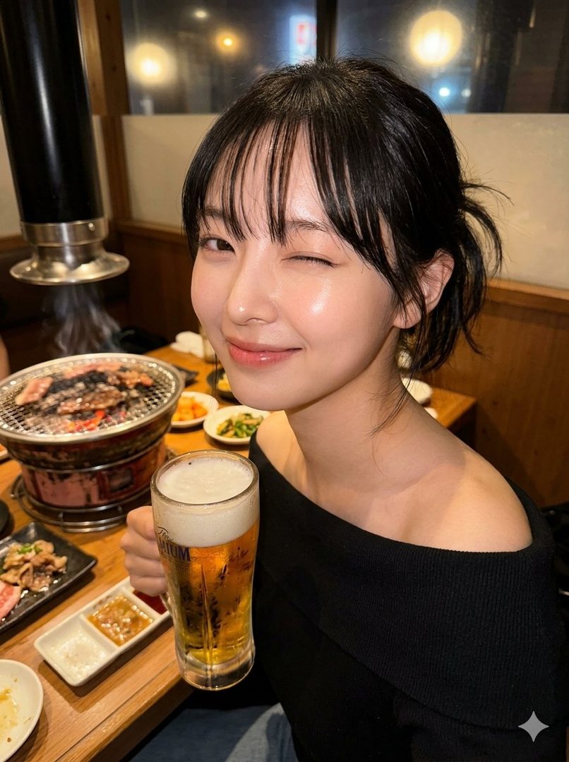 A young woman with black hair winks at the camera while holding a glass of beer in an indoor setting with a grill in the background.
