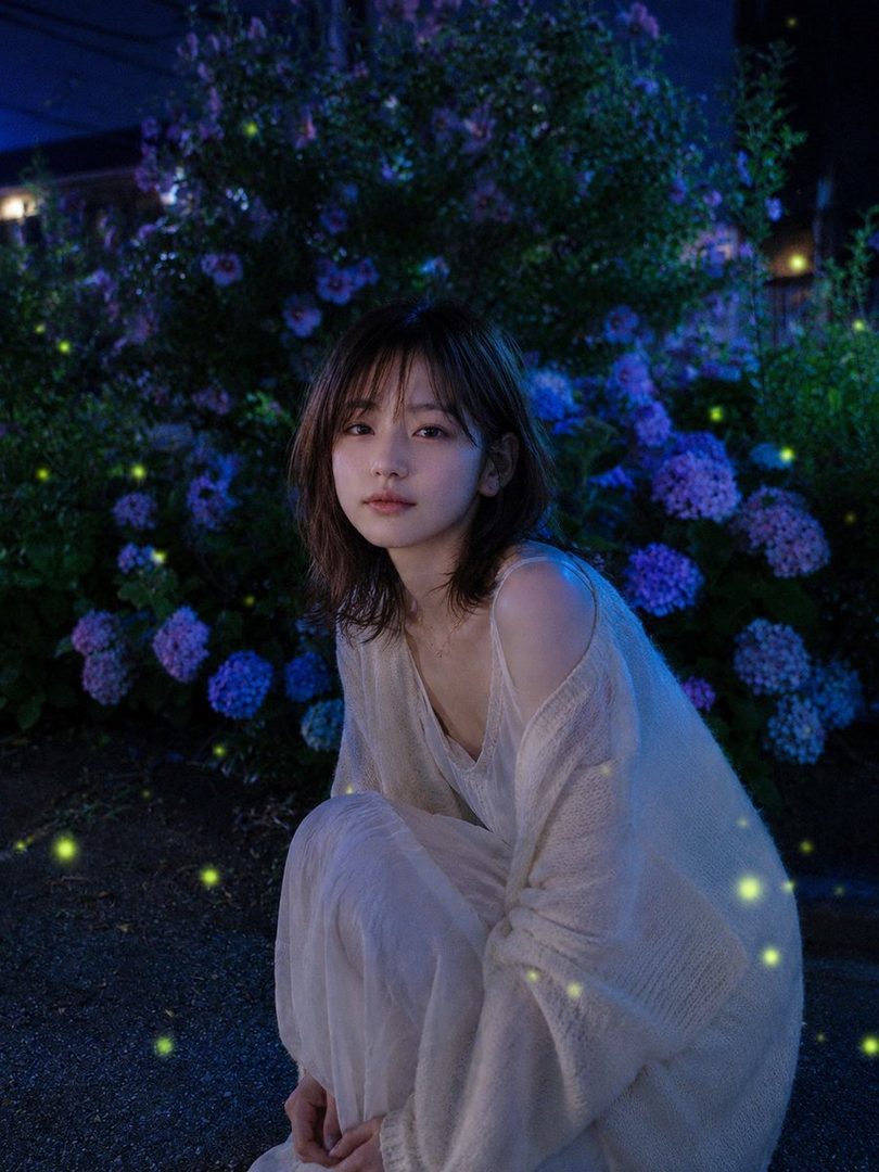 A young woman with brown hair in a white dress crouches in a magical night garden with glowing fireflies and purple hydrangeas.