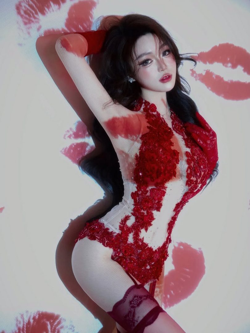 A woman in a red lace bodysuit and stockings poses against a white background with red lip prints projected onto it.