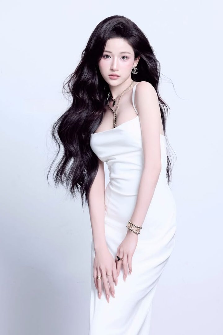 A beautiful woman with long black hair and a white dress poses elegantly in a studio setting.