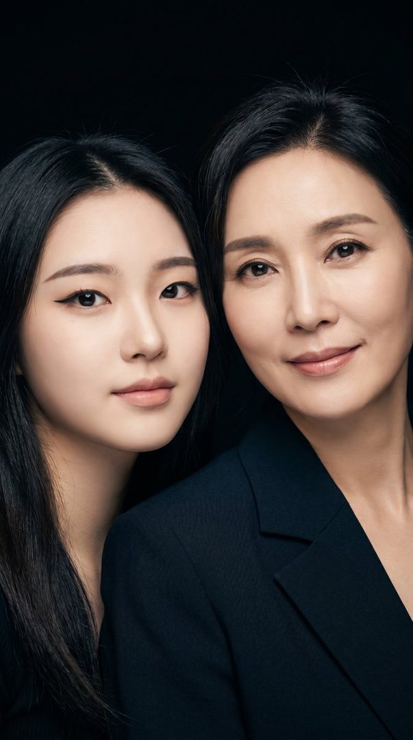 A photorealistic studio portrait of two Korean women, one younger and one older, both with black hair and wearing dark attire, against a black background.