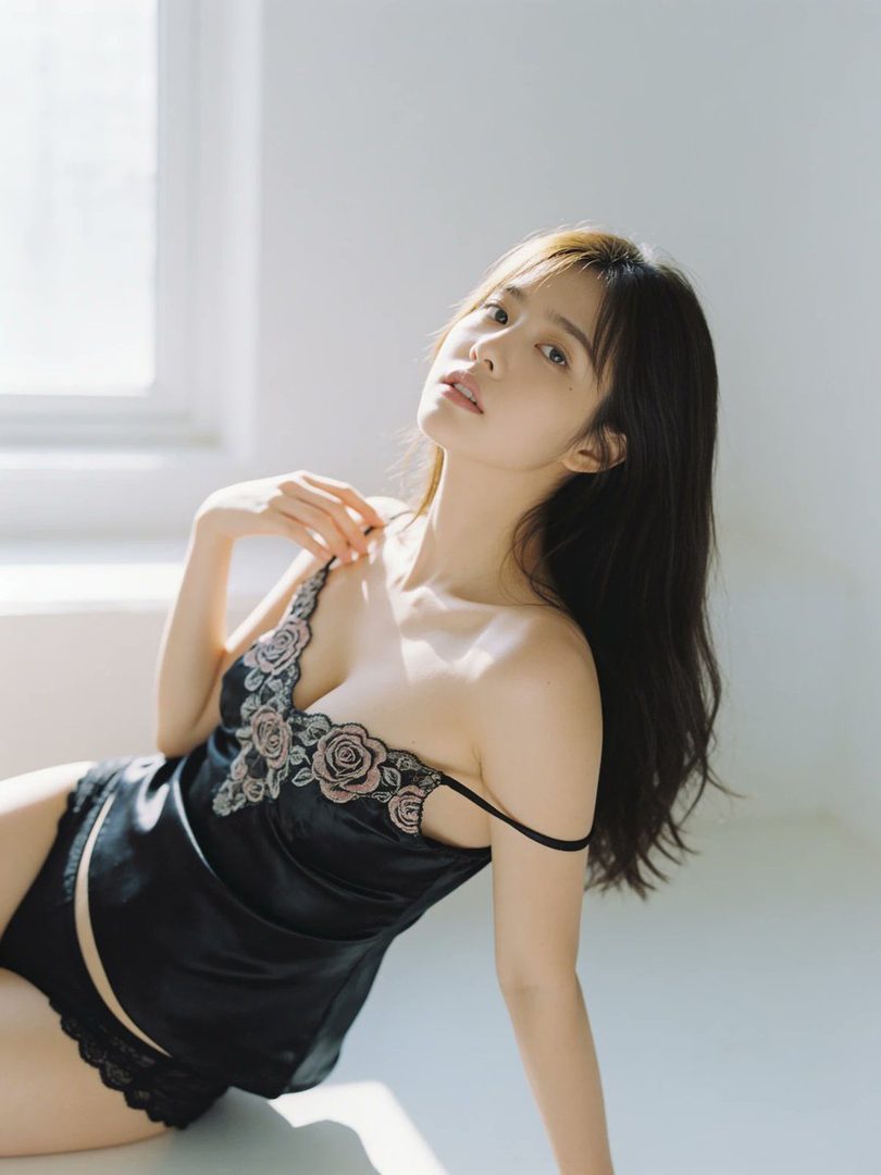 A beautiful woman with long brown hair is posing indoors, wearing a black top with floral embroidery.