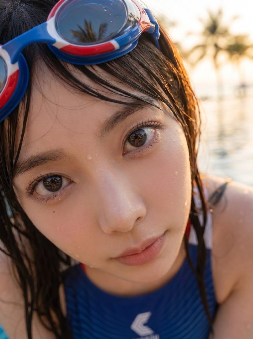 A close-up portrait of a young woman with wet black hair and swimming goggles on her head, looking directly at the camera with a fresh expression, with a pool and palm trees in the blurred background during golden hour.