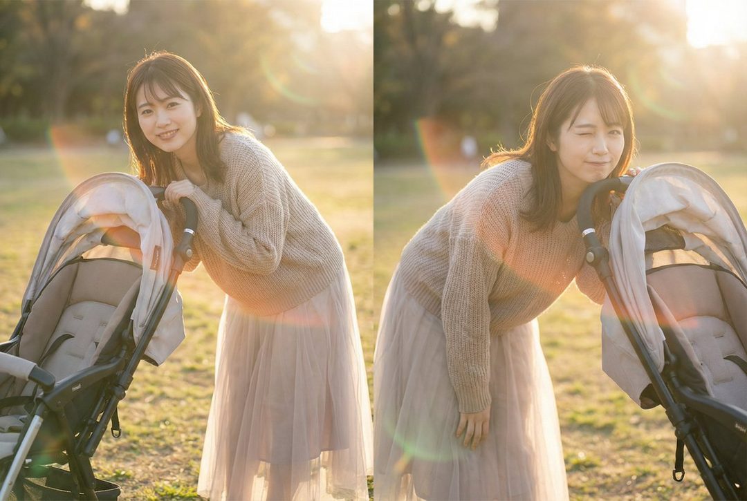 A young woman with brown hair and bangs, wearing a beige sweater and a light-colored skirt, smiles and winks while leaning on a baby stroller in an outdoor park during golden hour.