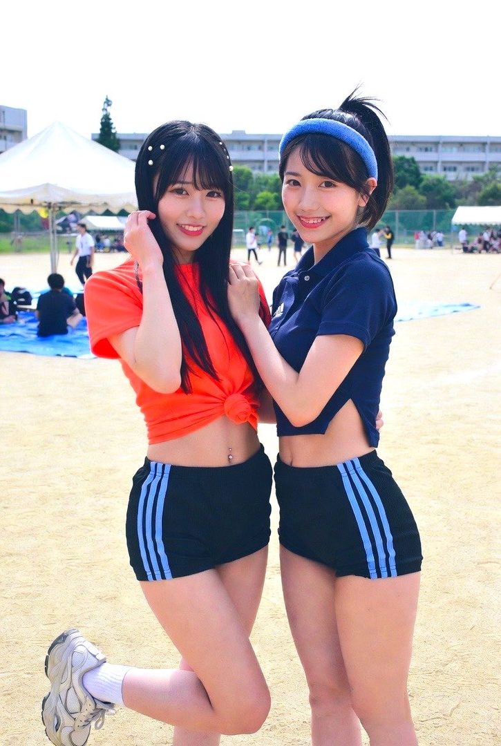 Two young Japanese women in sportswear pose on a school sports field, smiling at the camera.