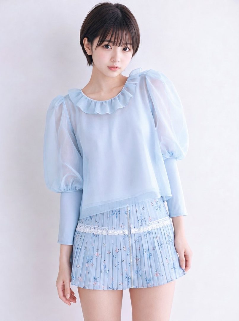 A young woman with short brown hair and bangs wears a light blue sheer blouse with ruffled collar and a pleated floral mini skirt.