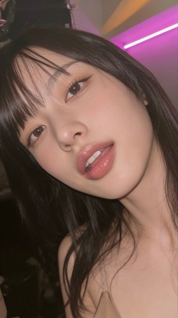 A close-up portrait of a woman with long dark hair and bangs, looking directly at the camera with slightly parted lips.