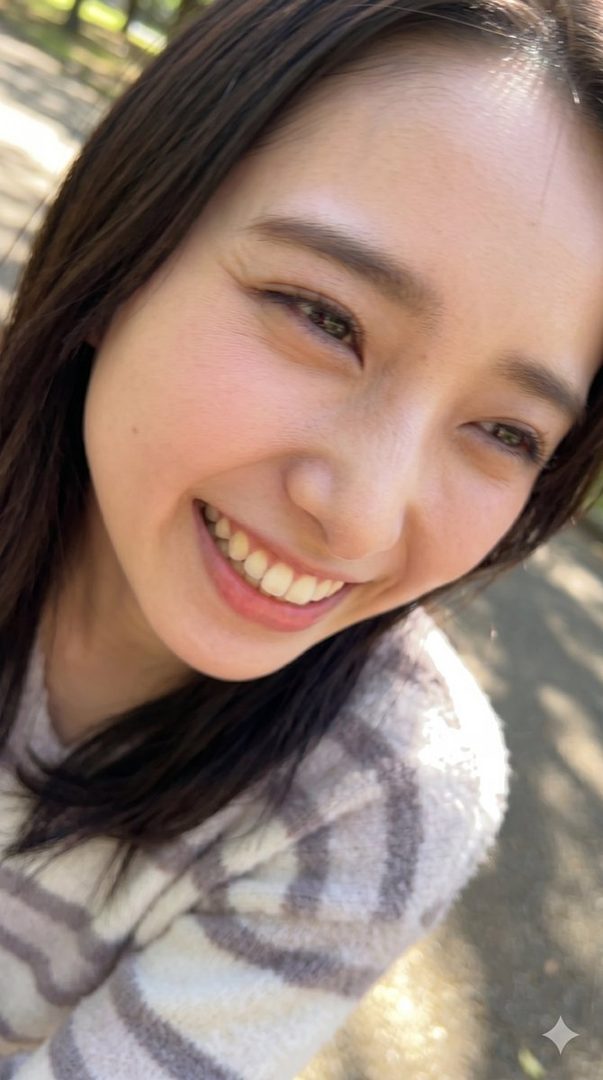 A close-up portrait of a smiling woman with dark brown hair wearing a striped sweater, captured outdoors in natural light.