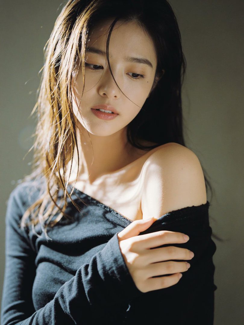 A photorealistic portrait of a woman with long brown hair and a black off-the-shoulder top, looking down with a serene expression.