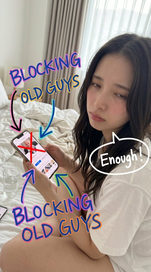 A young woman with dark wavy hair is lying in bed, looking annoyed while holding a smartphone with text overlays saying "Blocking Old Guys" and "Enough!".